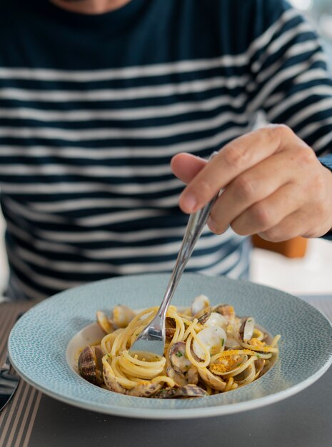 Foto detalhe masculino comendo macarrão espaguete com amêijoas e salmonete, comida mediterrânea