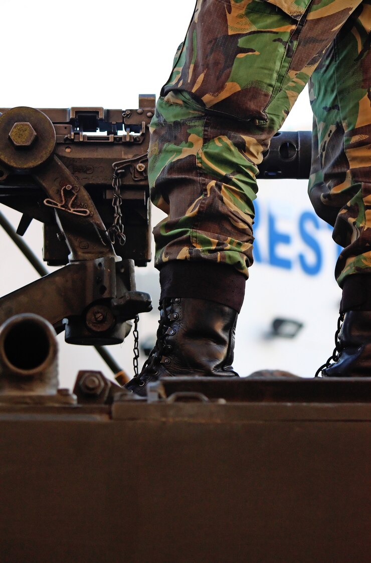 Foto detalhe montado da metralhadora e um pé e uma bota militares sobre um veículo.