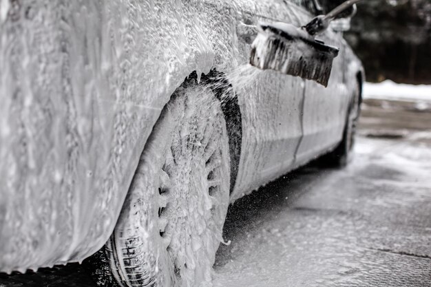 Detalhe no carro e no volante, coberto com muito sabão, pincel borrifando mais espuma de shampoo, ao ser lavado no lava-jato.