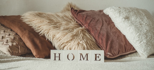 Detalhes da vida ainda no interior da sala de estar e a inscrição casa. muitas almofadas decorativas aconchegantes. descansar. conceito aconchegante de outono ou inverno, malhas. conceito de casa