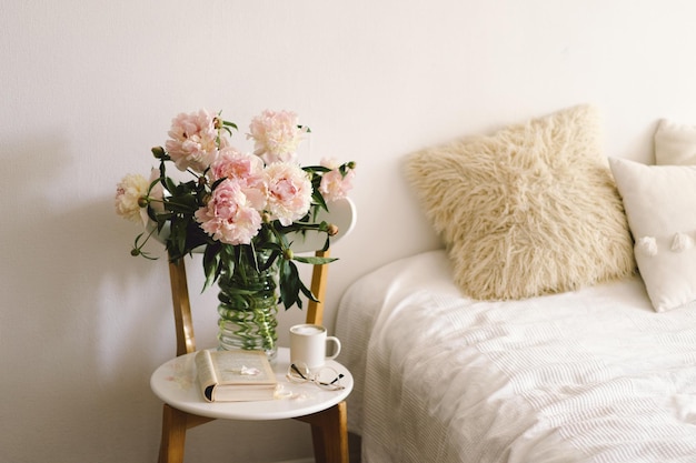 Detalhes da vida ainda no interior da sala de estar Livro aberto com copos xícara café e buquê flores peônias rosa brancas Leia e descanse Casa aconchegante