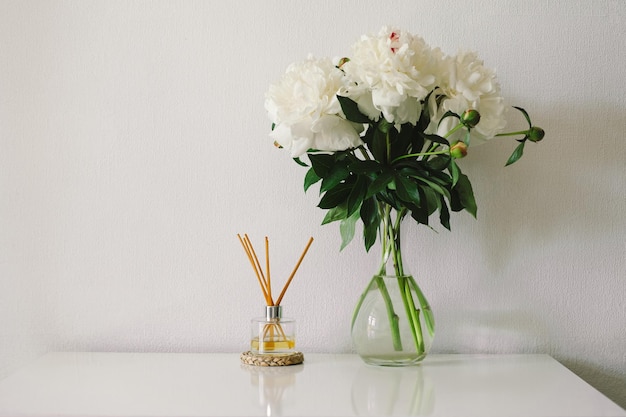 Detalhes de natureza morta no interior da sala de estar Paus de incenso e vaso com peônias brancas Fragrância ecológica para a casa Conceito de primavera aconchegante