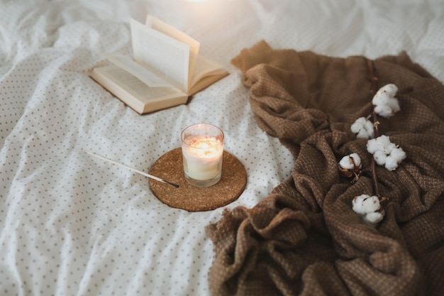 Detalhes interiores acolhedores da vida com uma vela de livro e um galho de algodão na cama macia e quente