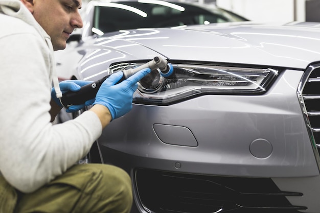 Detallado de automóviles - Trabajador con pulidora orbital en taller de reparación de automóviles. Enfoque selectivo.