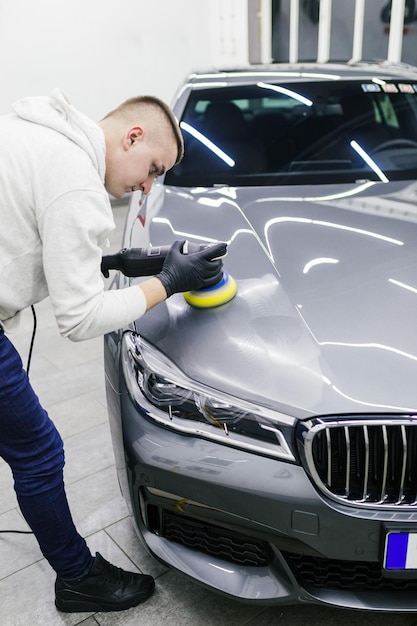 Detallado de automóviles - Trabajador con pulidora orbital en taller de reparación de automóviles.