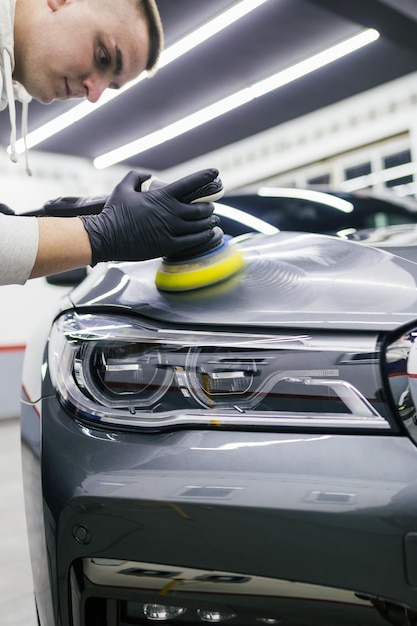 Detallado de automóviles - Trabajador con pulidora orbital en taller de reparación de automóviles.