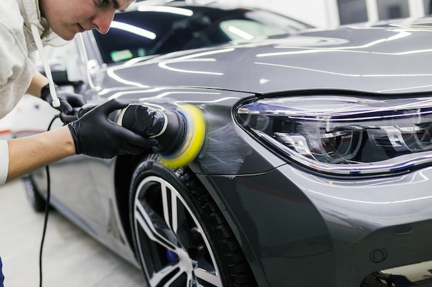 Detallado de automóviles - Trabajador con pulidora orbital en taller de reparación de automóviles.