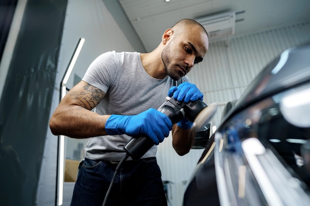 Detallando el coche. Manos masculinas con pulidor orbital en taller de reparación de automóviles, cerrar