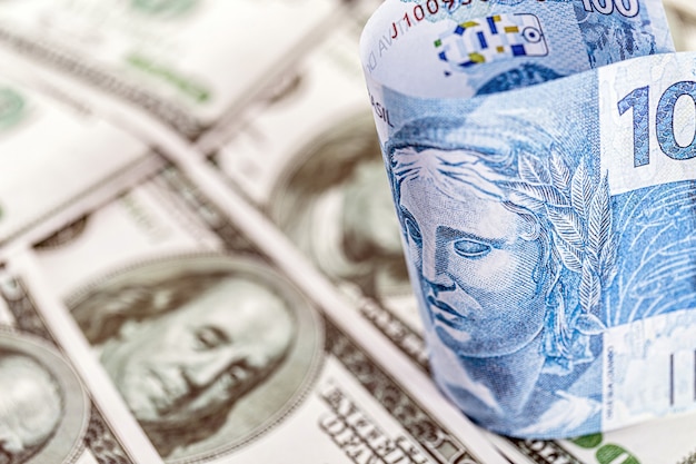 Detalle de un billete de cien reales de brasil, atrapado entre billetes de 100 dólares americanos