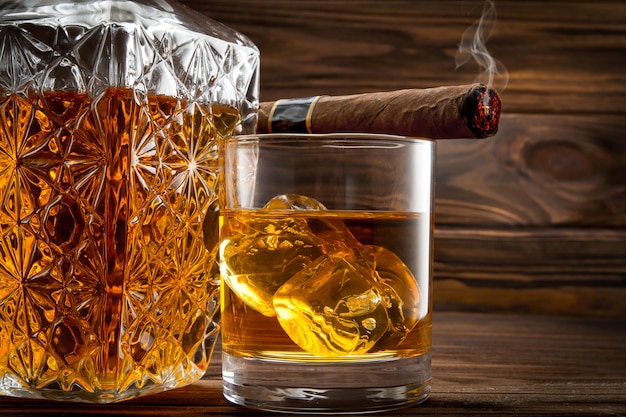 Detalle de botella, vaso con whisky y cigarro humeante.