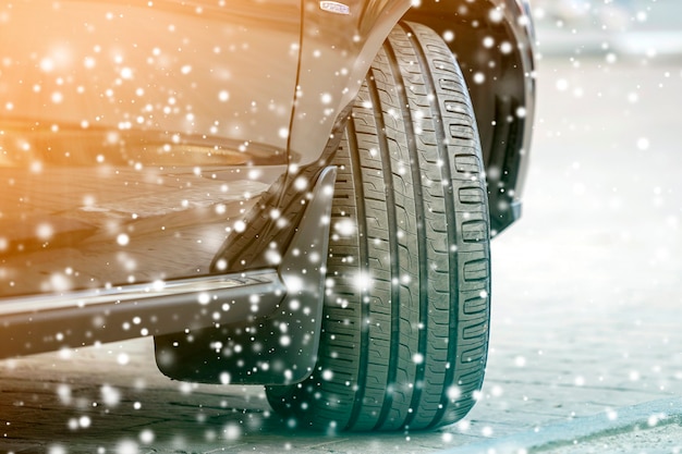 Detalle de detalle de la rueda del coche con el nuevo protector de neumáticos de caucho negro en la carretera cubierta de nieve en invierno. Concepto de transporte y seguridad.