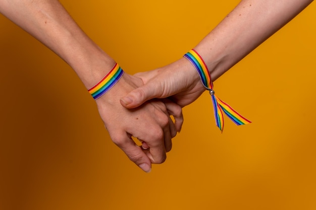 Detalle de dos manos de dos mujeres dándose la mano con un concepto LGBT de pulsera sobre un fondo amarillo un par de chicas lesbianas