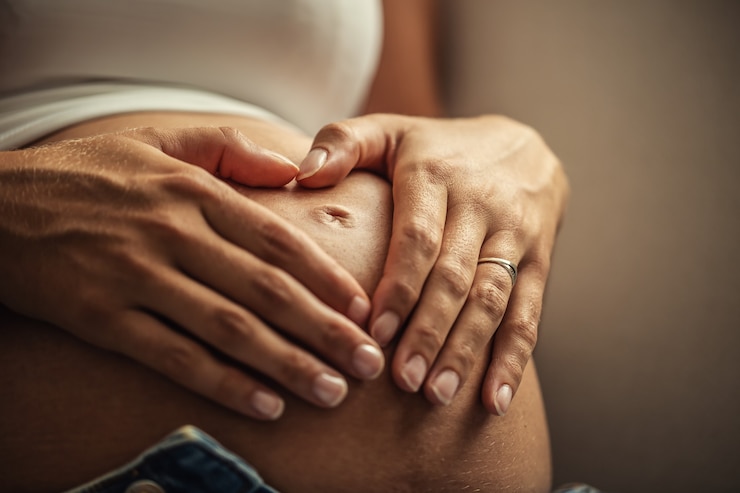 Foto detalle de las dos manos de la mujer colocadas sobre su vientre embarazado.