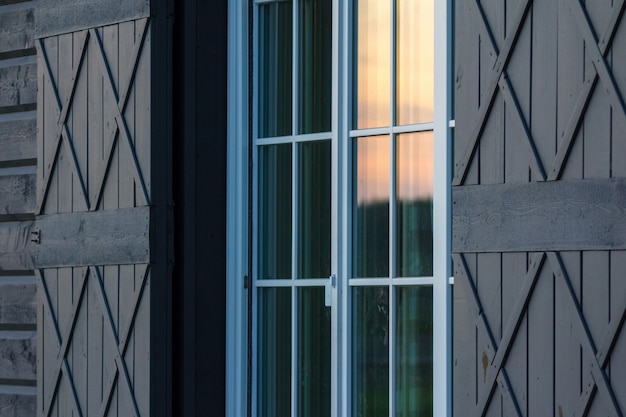 Detalle del exterior de la casa de madera. Reflexión de la luz del atardecer cálido en las ventanas de vidrio.