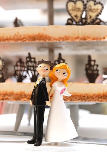 Foto detalle de las figuras de la novia y el novio junto al pastel de bodas