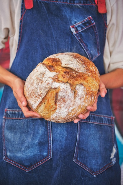 Detalle de la foto de manos femeninas sosteniendo un pan artesanal partido por la mitad con un delantal de cocina azul.