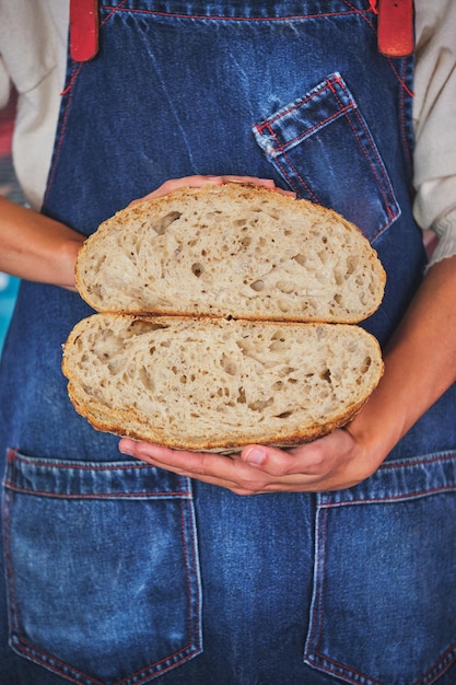 Detalle de la foto de manos femeninas sosteniendo un pan artesanal partido por la mitad con un delantal de cocina azul.