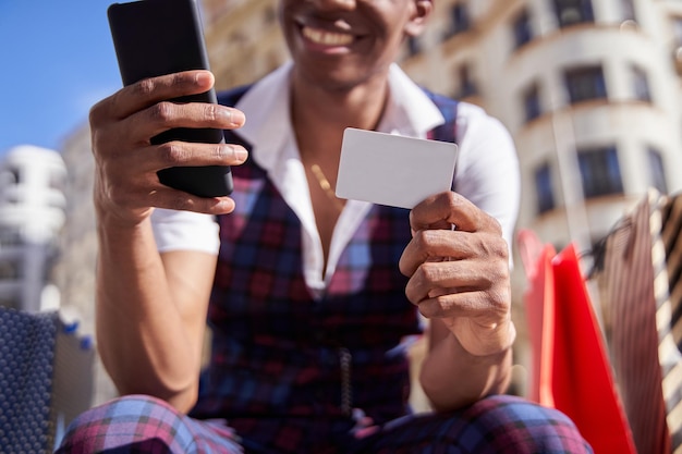 Detalle de un hombre afroamericano con una tarjeta de crédito haciendo compras a través de un enfoque selectivo de teléfonos inteligentes