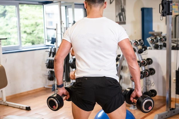 Detalle de un hombre caucásico en el gimnasio con una camiseta blanca levantando pesas vida sana y saludable haciendo deporte