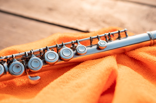 Detalle de la llave de flauta plateada que brilla a la luz del atardecer sobre tela naranja