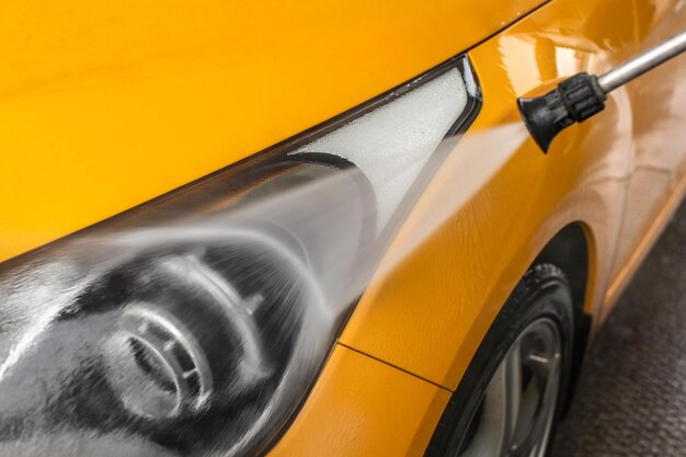 Detalle de la luz delantera del coche amarillo oscuro que se lava con chorro de agua en el lavado de coches.