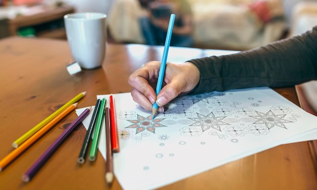 Detalle de la mano de una mujer coloreando mandalas mientras toma un té en el salón