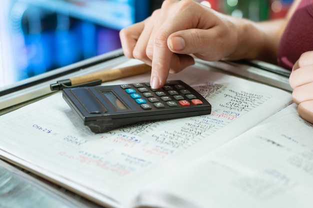 detalle de la mano de una mujer usando su pequeña calculadora y un bolígrafo de cartón ecológico en un cuaderno