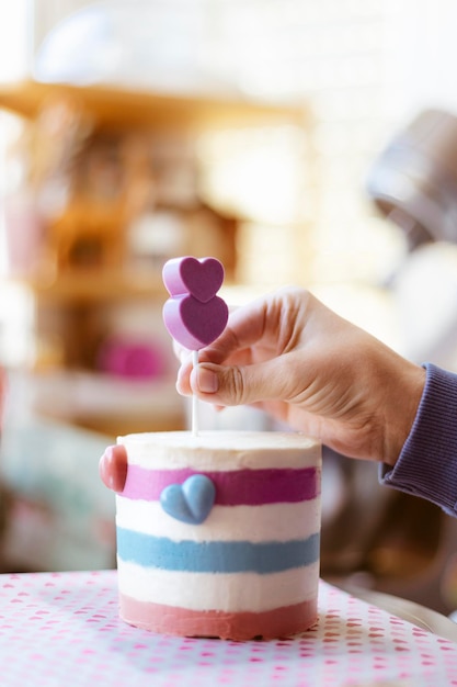 Detalle de la mano de una persona decorando un pastel para el Día de San Valentín. Primer plano, enfoque selectivo. Espacio para texto.