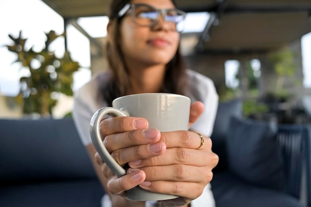 Detalle de las manos de la mujer sosteniendo una taza de café fondo desenfocado de la empresaria tomando un descanso