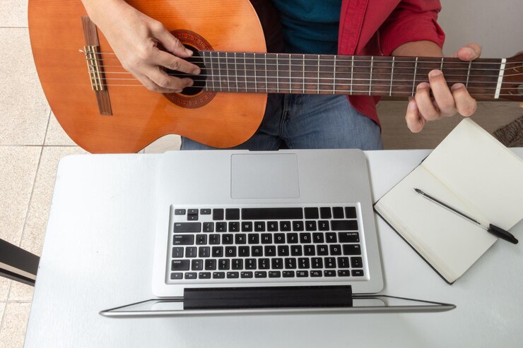 Foto detalle de unas manos tocando la guitarra frente a una laptop