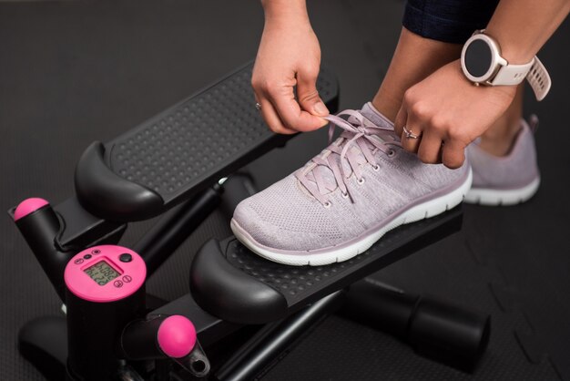 Detalle de mujer atando sus zapatillas para entrenar en casa con paso a paso