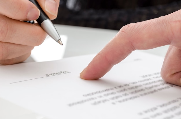 Foto detalle de una mujer firmando un papel. dedo masculino mostrando dónde firmar.