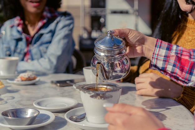 Detalle de una mujer irreconocible que sirve té en un café al aire libre en otoño