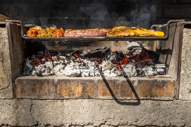 Detalle de la parrilla de la comida de una barbacoa con salchichas y brochetas de pollo en un día soleado en el campo y algunas pinzas sosteniendo un trozo de pollo bajo ángulo de visión