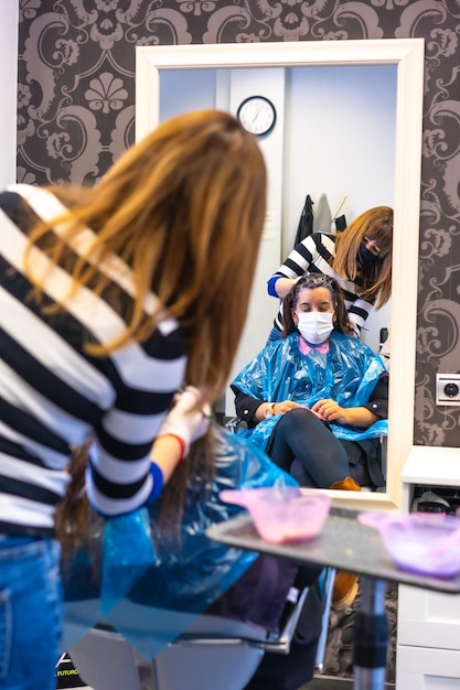 Detalle de Peluquero con mascarilla aplicando el tinte al cliente con mascarilla