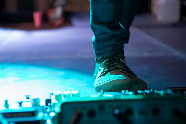 Detalle del pie a punto de pisar los pedales de la guitarra eléctrica en el escenario de un concierto de música por la noche