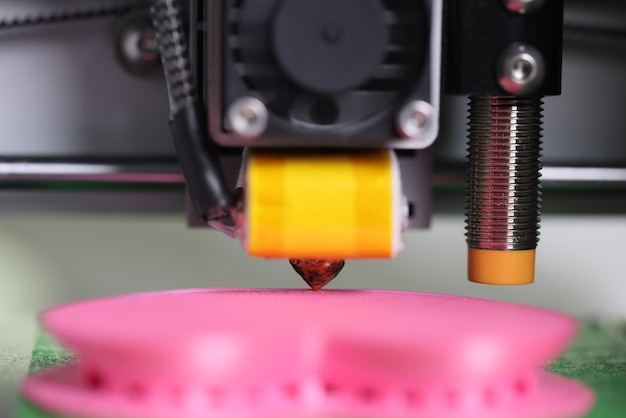 Un detalle en primer plano de la impresora d y un modelo rosado de un modelo tridimensional trabajando