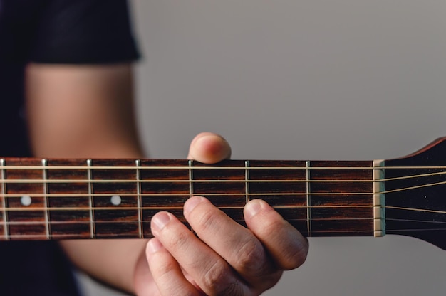 Detalle de primer plano de la mano masculina en el cuello de la guitarra acústica haciendo acordes con espacio de copia