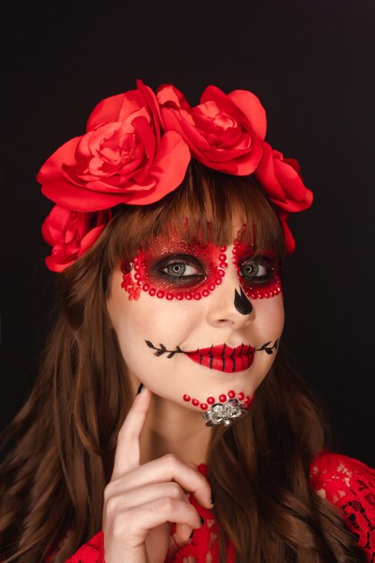 Detalle del retrato del rostro de una joven con maquillaje del Día de Muertos sobre fondo negro.