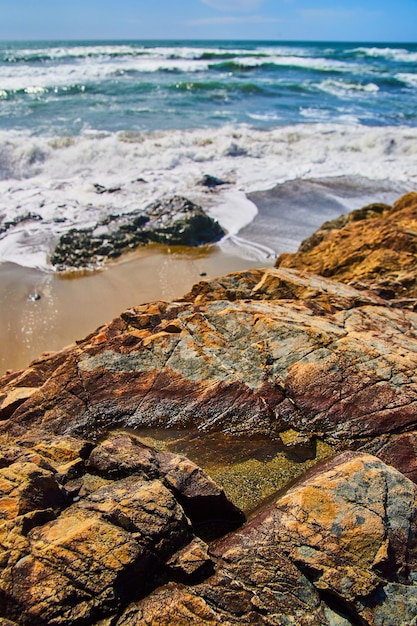 Detalle de roca con charco de agua en la playa de arena con olas rompiendo