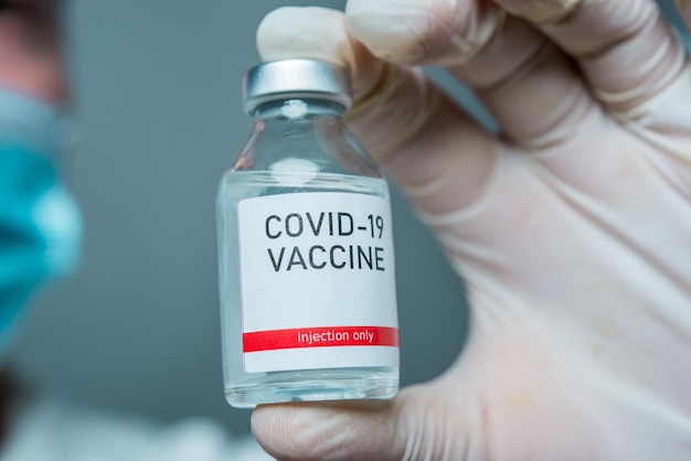 Detalle de la vacuna para Covid-19 entregando las manos del científico con máscara protectora.