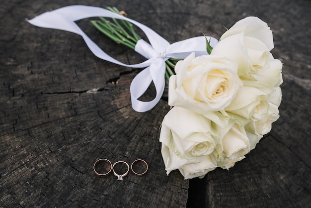 Foto detalles de boda decoración de boda anillos de boda con diamantes y ramo de rosas blancas sobre fondo de madera