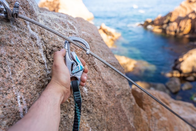 Detalles de las garras de escalada la mano del joven en las rocas sobre el mar con cuerda y casco