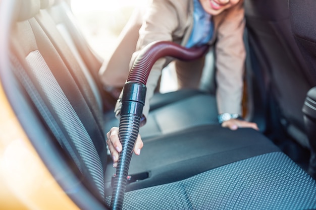 Detalles del interior del coche. Feliz empresaria limpia el interior de su coche con aspiradora.