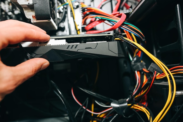 Detalles internos de la computadora personal. El hombre está limpiando cables con guantes amarillos. Placa base y tarjeta de video en el polvo. PC rota.