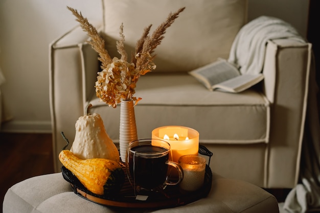 Detalles de naturaleza muerta en el interior de la casa de la sala de estar. Calabaza y taza de té con velas en una bandeja para servir. Descanso y lectura. Otoño acogedor