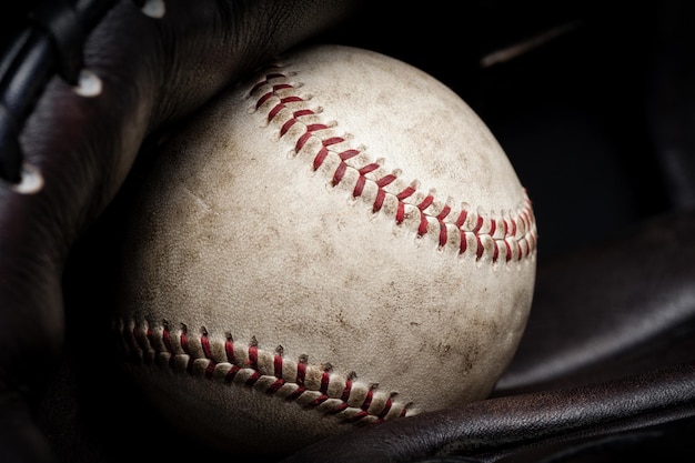 Detalles de primer plano del viejo béisbol en la palma de un guante de béisbol marrón oscuro