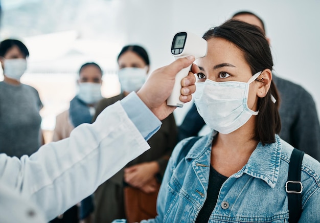 Detección de covid con una turista con una máscara a la que se le toma la temperatura con un termómetro infrarrojo mientras espera para embarcar en un aeropuerto Restricciones de viaje durante la pandemia del virus de la corona