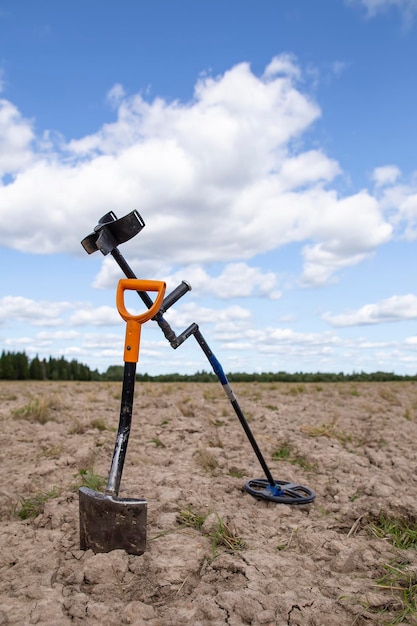 Detector de metales y pala en un campo sobre un fondo de bosque y cielo azul con nubes