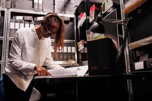 Detektivin liest Kriminalakten, analysiert Zeugenaussagen und sucht nach Einsichten. Afroamerikanischer Polizist studiert kriminologische Schlussfolgerungen im Büroraum des Ermittlers